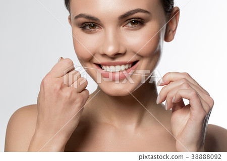 Joyful young woman holding dental floss near mouth 38888092