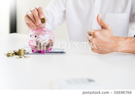Close up of Businessman putting coin into small piggy bank , The 38896766