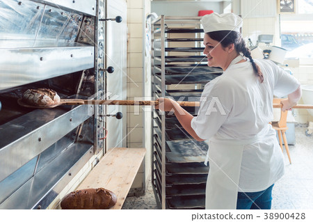 Baker woman getting bread out of bakery oven Baker woman getting bread out of bakery oven 38900428