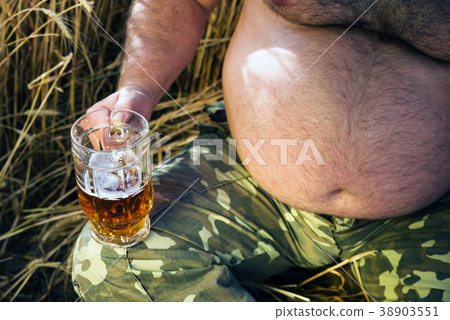 large glass of light beer is held by a fat man 38903551