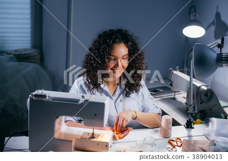 smiling seamstress sitting and holding beads in 38904013