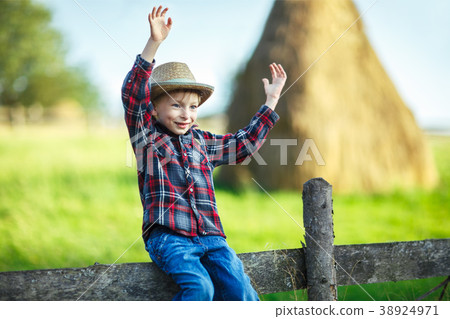 Kid boy in straw hat balances on wooden hedge, close-up 38924971
