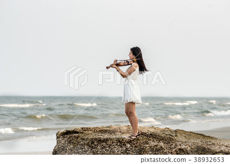 Happy woman playing violin on the beach. 38932653