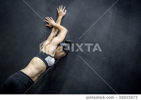 young asian woman stretching arm on black wall 38935873