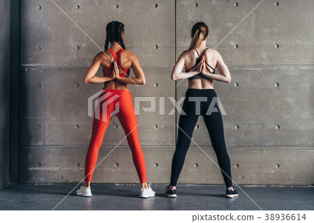 Fit women stretching, holding Anjali Mudra behind Fit women stretching, holding Anjali Mudra behind 38936614