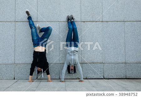 Two hipsters doing handstand against wall in city 38948752