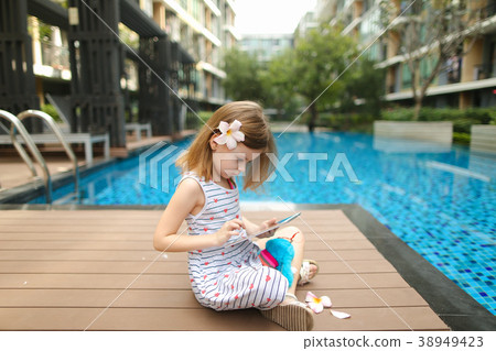 little girl uses tablet sitting close to swimming 38949423