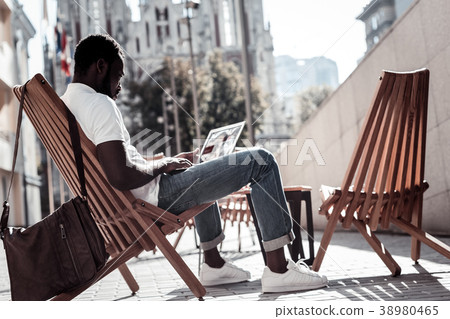 Serious millennial guy working on laptop outdoors Serious millennial guy working on laptop outdoors 38980465