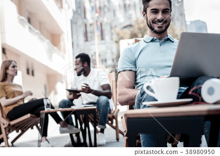 Cheerful young man smiling while working on laptop Cheerful young man smiling while working on laptop 38980950