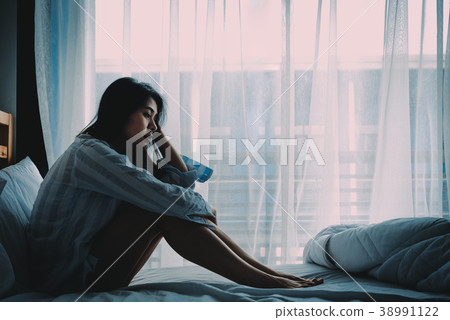 Asian woman sitting on a bed looking sad Asian woman sitting on a bed looking sad 38991122