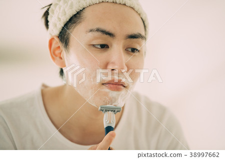 刮他的鬍子的一個年輕人 38997662