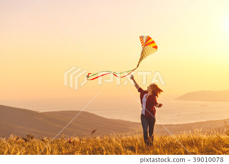 Happy young woman running with kite on glade at sunset in summer Happy young woman running with kite on glade at sunset in summer 39010078