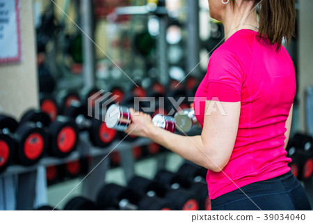 Back view young woman trains biceps in gym Back view young woman trains biceps in gym 39034040