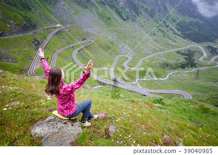 Young female lifting hands to the sky admiring the beauty of winding Transfagarashan road in Romania Young female lifting hands to the sky admiring the beauty of winding Transfagarashan road in Romania 39040985