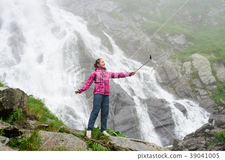 Woman taking a selfie in front of big waterfall. 39041005