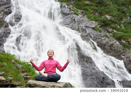 Woman meditating relaxing alone against waterfall Balea Woman meditating relaxing alone against waterfall Balea 39041019