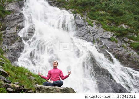 Woman meditating relaxing alone against waterfall Balea Woman meditating relaxing alone against waterfall Balea 39041021