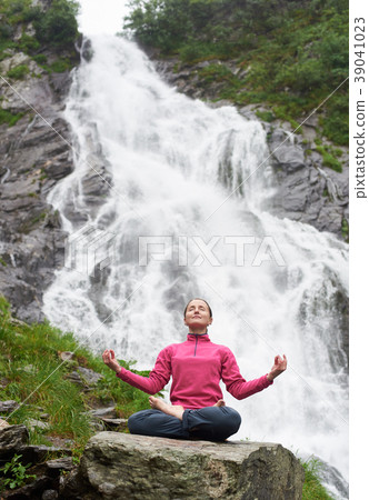 Woman practising yoga on stone in front of beautiful Balea waterfall in Romania 39041023