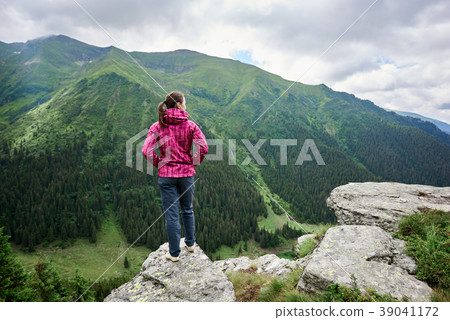 Rear view of girl standing on cliff against mighty mountains 39041172