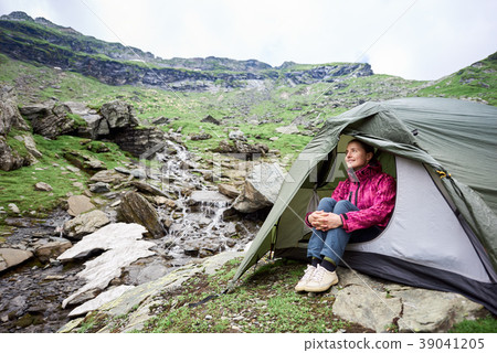 Happy tourist female sits in tent near mountain stream 39041205