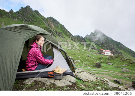 Happy tourist female sits in tent near mountain stream Happy tourist female sits in tent near mountain stream 39041206
