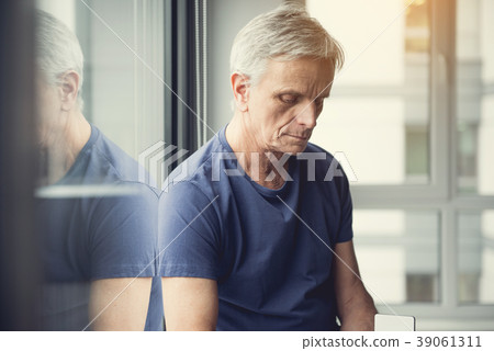 Sad mature man sitting on windowsill Sad mature man sitting on windowsill 39061311