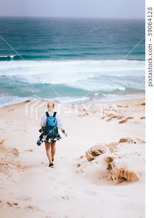 Woman hiker with backpack going down a sand dune Woman hiker with backpack going down a sand dune 39064128