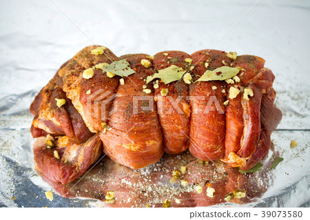 Raw marinated pork roll sprinkled with spices. 39073580