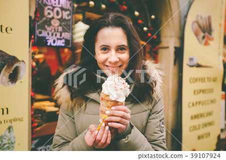 A beautiful girl in a warm jacket eats trdelnik or 39107924