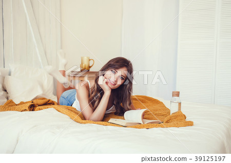 woman lying in bed while reading a book woman lying in bed while reading a book 39125197