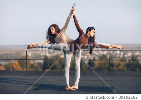Two beautiful women doing yoga asana virabhadrasana on the roof 39152162
