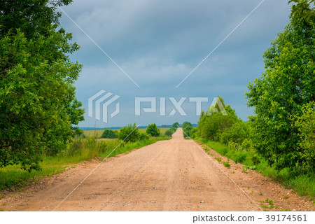 the unpaved road is empty, the sky is dark clouds 39174561
