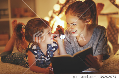 mother and child daughter reading a book and a flashlight before 39202073