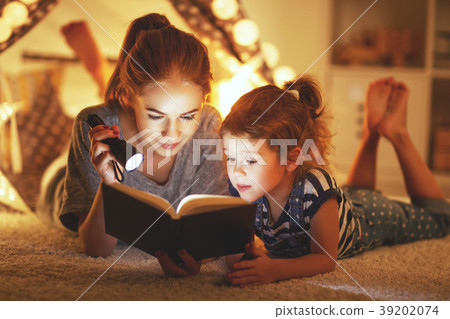 mother and child daughter reading a book and a flashlight before 39202074