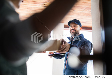 Woman receiving parcel from delivery man at the Woman receiving parcel from delivery man at the 39217789