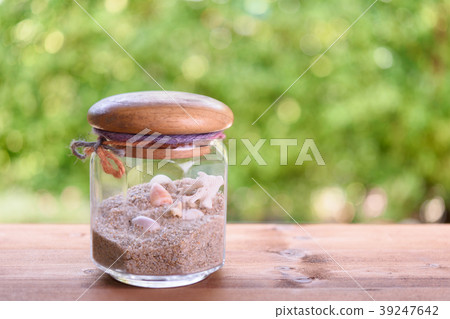 Sheshells and sand in glass jar on wood table Sheshells and sand in glass jar on wood table 39247642