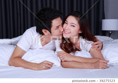 man is kissing his beautiful smiling wife in cheek on bed 39275523