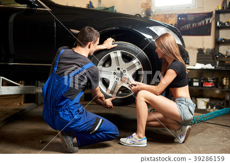 Woman helps an auto mechanic repair front wheel of car 39286159