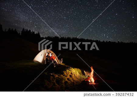 Tourists near campfire and tents under starry sky Tourists near campfire and tents under starry sky 39287432