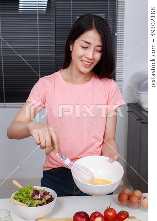 woman cooking and whisking eggs in a bowl in kitchen woman cooking and whisking eggs in a bowl in kitchen 39302188