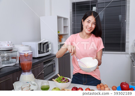 woman cooking and whisking eggs in a bowl in kitchen woman cooking and whisking eggs in a bowl in kitchen 39302189
