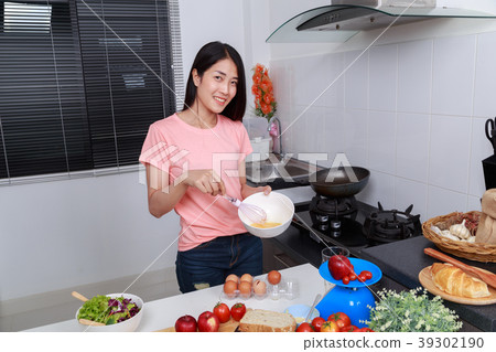woman cooking and whisking eggs in a bowl in kitchen 39302190