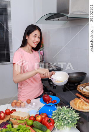 woman cooking and whisking eggs in a bowl in kitchen woman cooking and whisking eggs in a bowl in kitchen 39302191