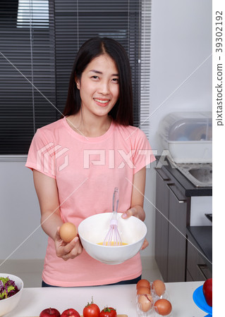 woman cooking and whisking eggs in a bowl in kitchen woman cooking and whisking eggs in a bowl in kitchen 39302192