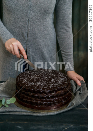 Woman cuts chocolate cake close. Dark tones 39317562