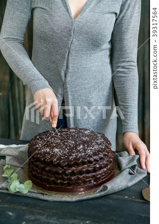 Woman cuts chocolate cake close. Dark tones 39317564
