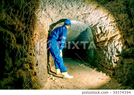 Hunched worker in overall and helmet underground Hunched worker in overall and helmet underground 39374394