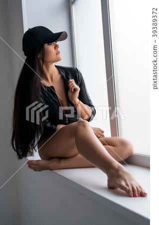 Sexy brunette in black baseball cap on window sill Sexy brunette in black baseball cap on window sill 39389372
