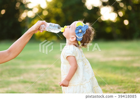 little girl drinks water bottle mothers hand little girl drinks water bottle mothers hand 39418085