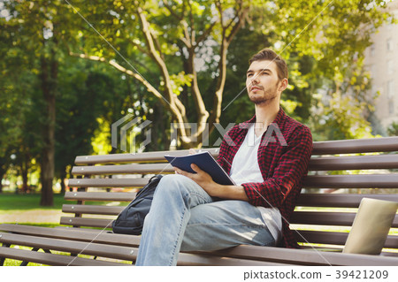 Young man thinking with a copy-book outdoors 39421209